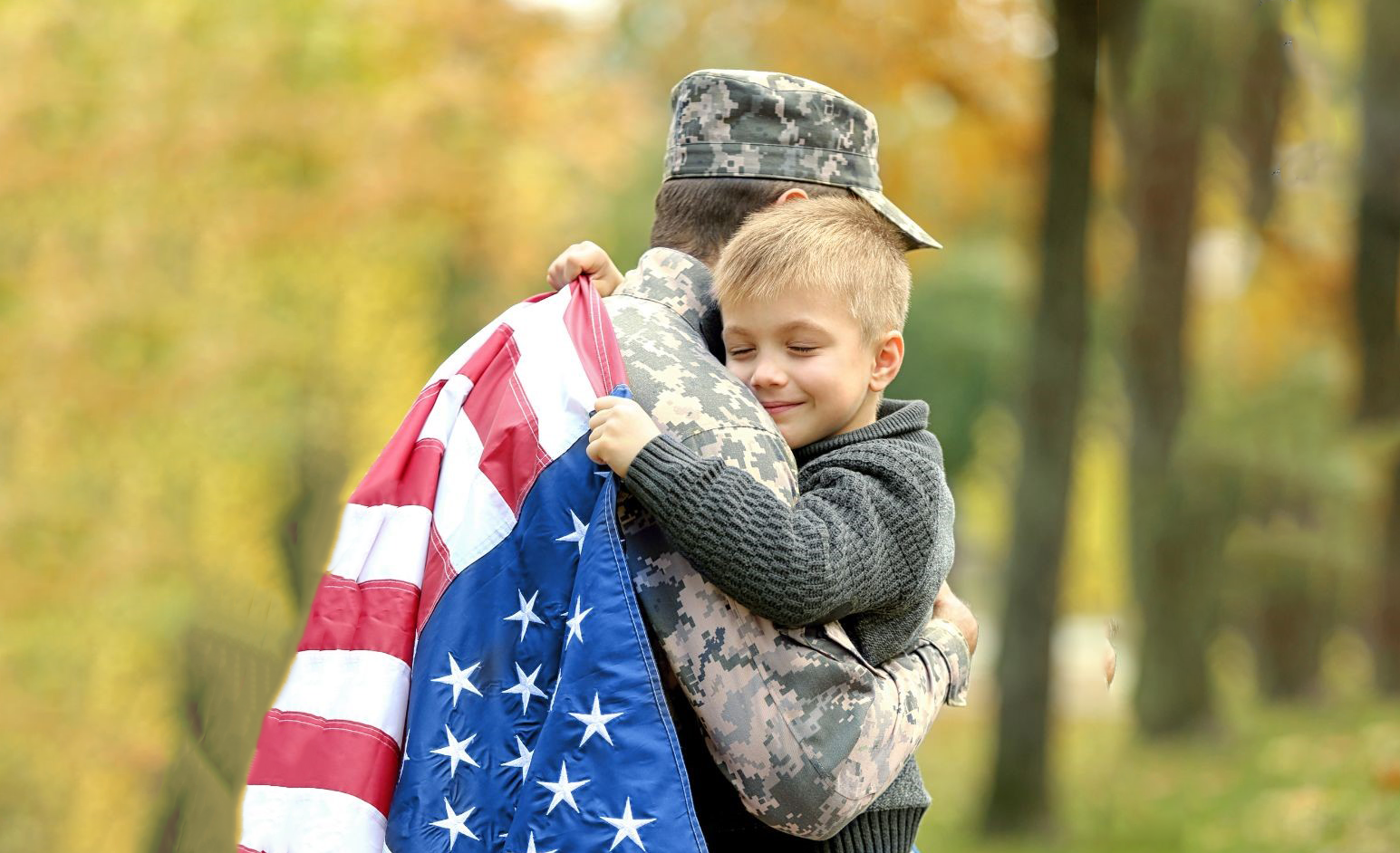boy hugging a military and holding a U.S flag