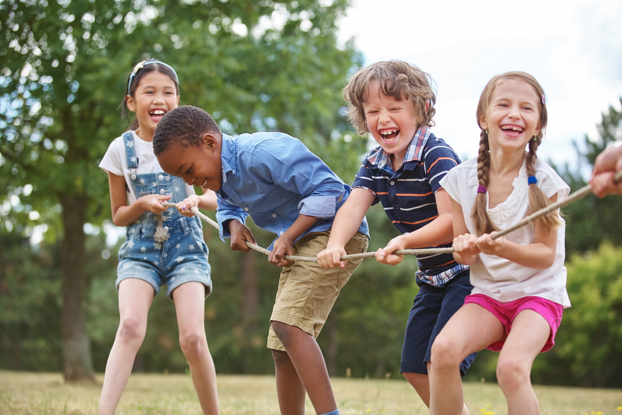 Children joyfully play tug-of-war in a green park, showcasing teamwork and laughter in a lively outdoor setting.